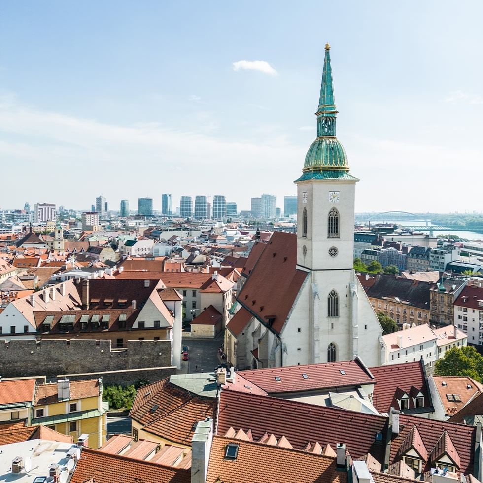 A cityscape with historic buildings and a prominent church tower during Bratislava Carnival.