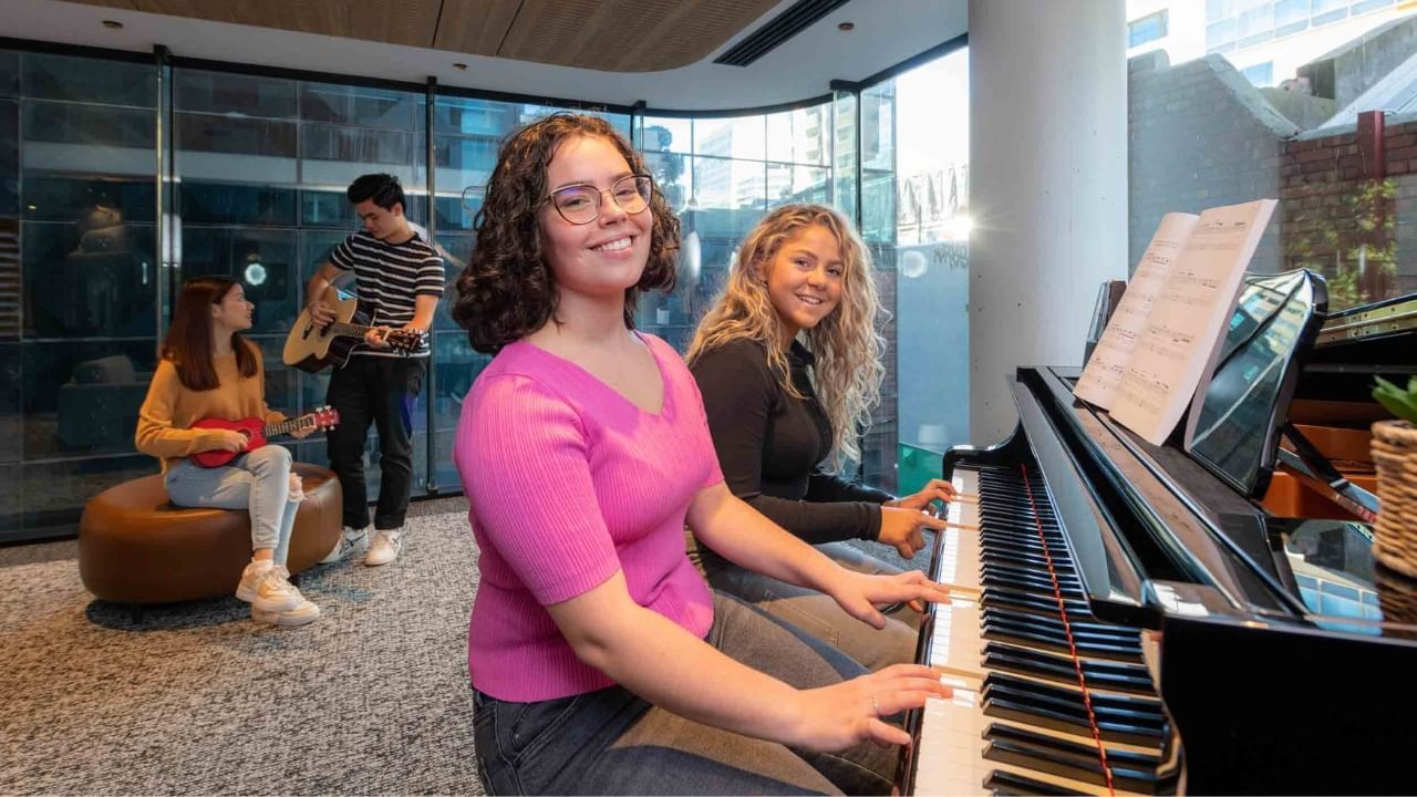 A group of students are playing music together with piano and guitars in a room.