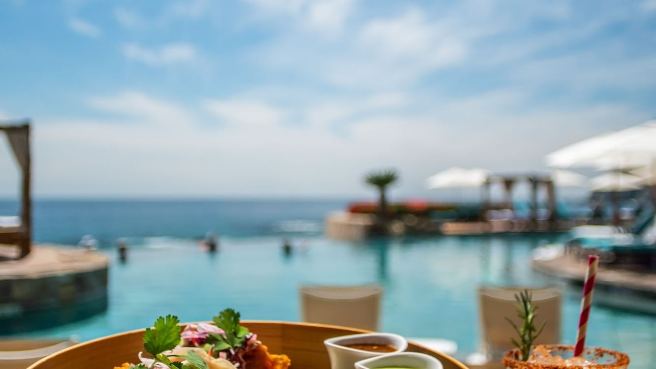 Basket of fish tacos and sauces, with a drink beside the infinity pool in Sirenas Restaurant at Hacienda Del Mar Los Cabos.