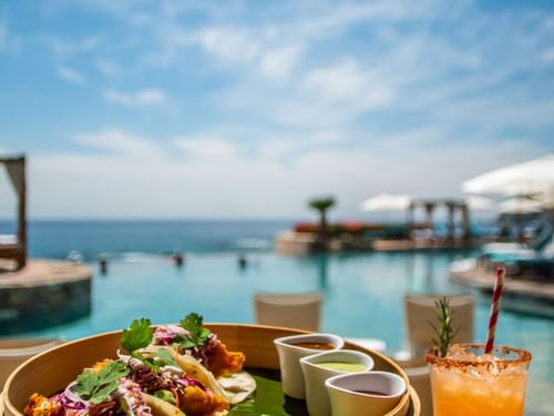 Basket of fish tacos and sauces, with a drink beside the infinity pool in Sirenas Restaurant at Hacienda Del Mar Los Cabos