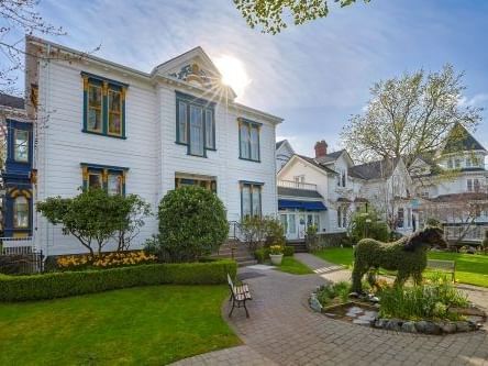 White two-story historic house with manicured gardens and topiary under a bright blue sky at Belleville House