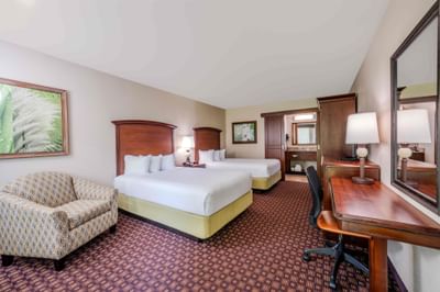 Spacious double queen guestroom with patterned carpet, work desk, and tropical artwork at Rosen Inn International