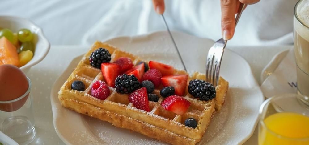Guest eating a berry waffle under the covers for in-room breakfast at Warwick Corporate