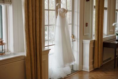 White wedding dress hanging from glass doors between golden curtains at Spencer Hotel & Conference Centre