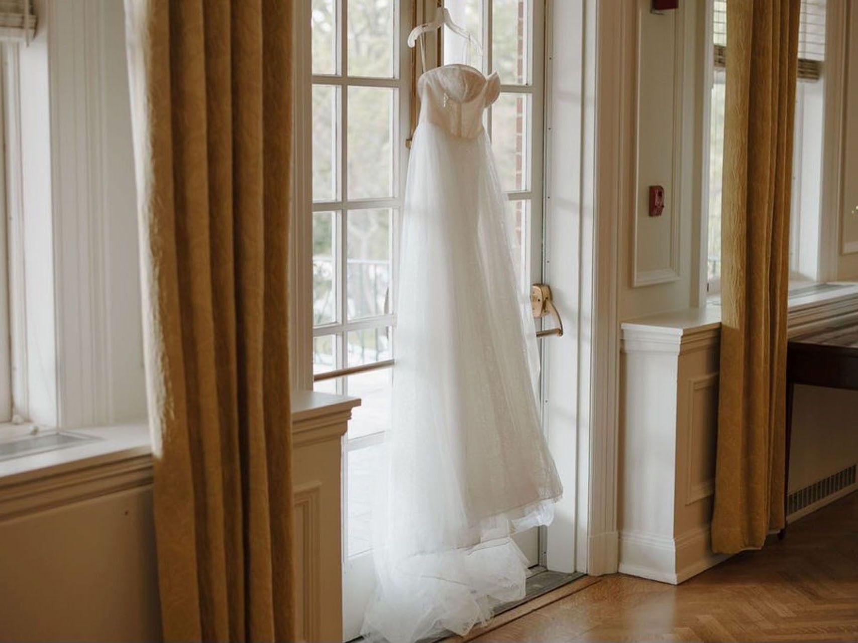 White wedding dress hanging from glass doors between golden curtains at Spencer Hotel & Conference Centre