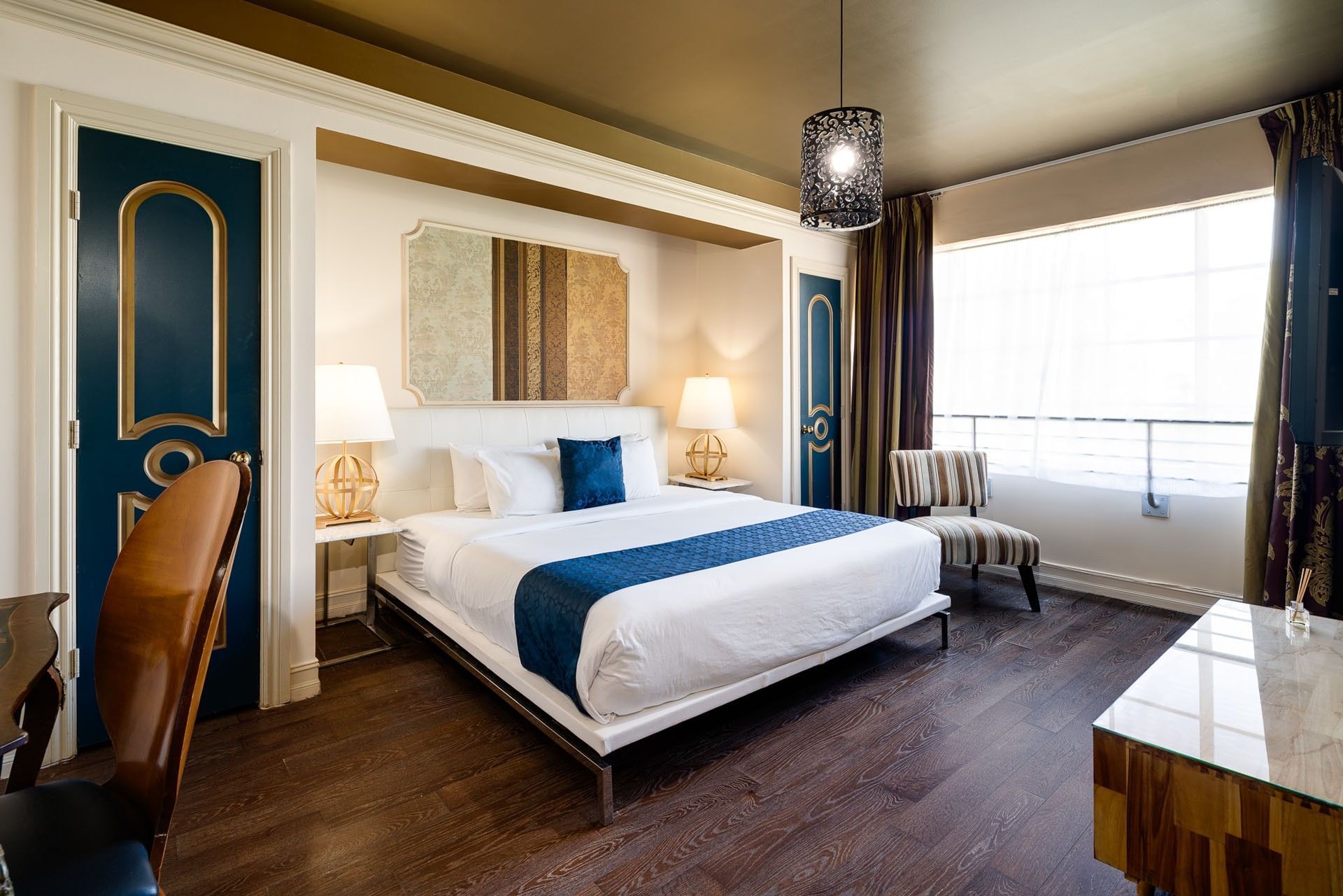 A hotel room with a king-sized bed, desk, chair, and window