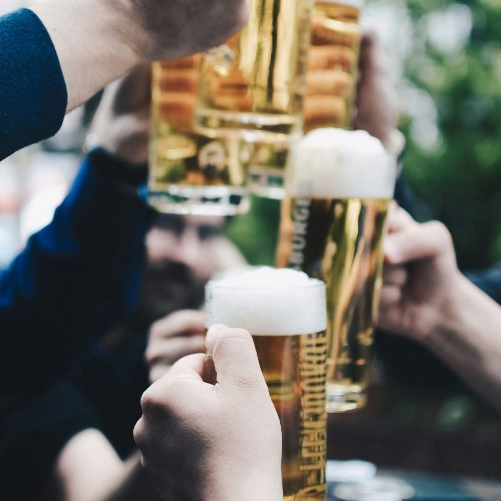 People raising glasses of beer with the brand name Augustiner visible on one of the glasses.