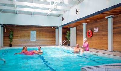 Guests relaxing in an indoor swimming pool by wooden walls under a bright skylight at Rodd Brudenell River Resort