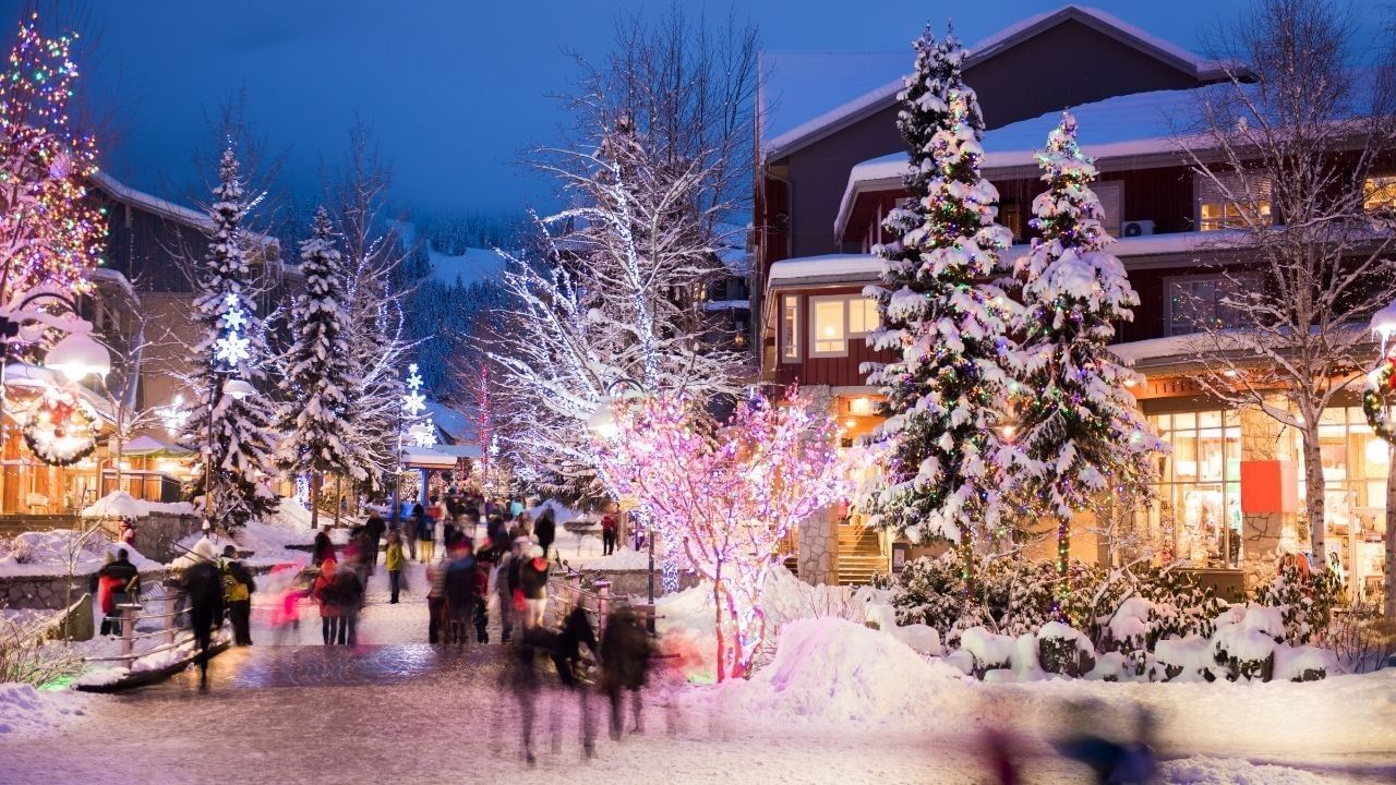 People walking on snowy streets with Christmas lights and trees at night.