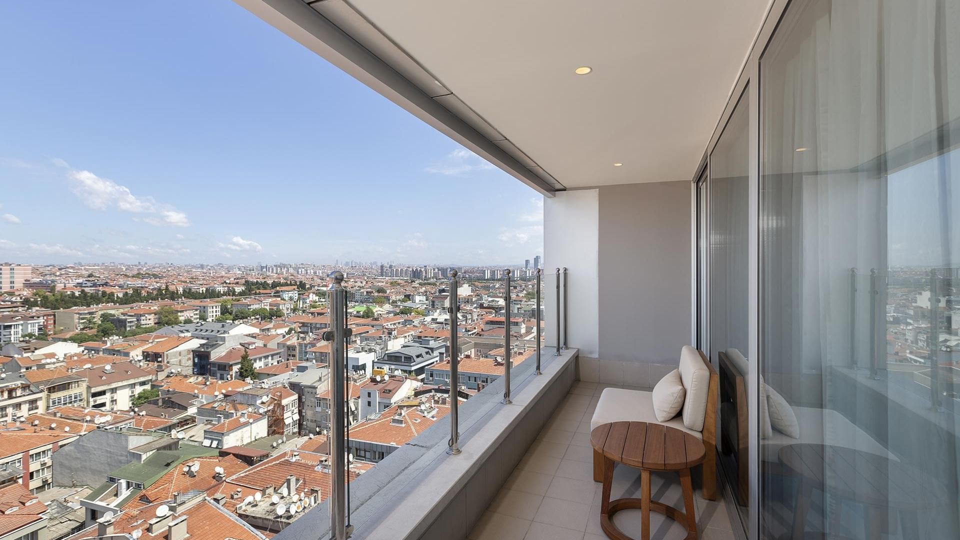 A balcony with a wooden table and a couch overlooking a cityscape filled with buildings under a clear sky in Junior Suite at Titanic Port Bakırköy