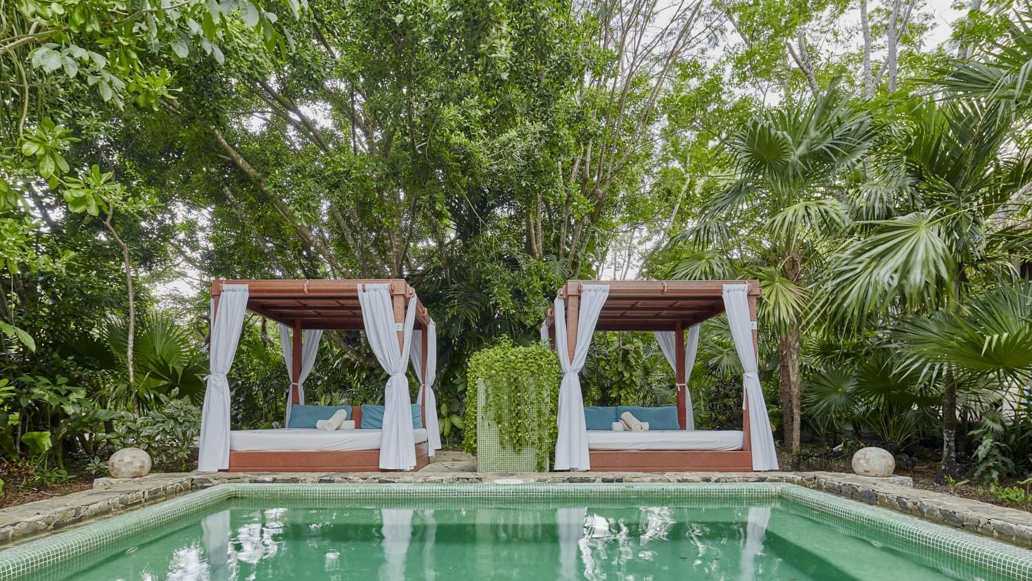 Two canopy beds by the outdoor pool with lush greenery at The Explorean Cozumel