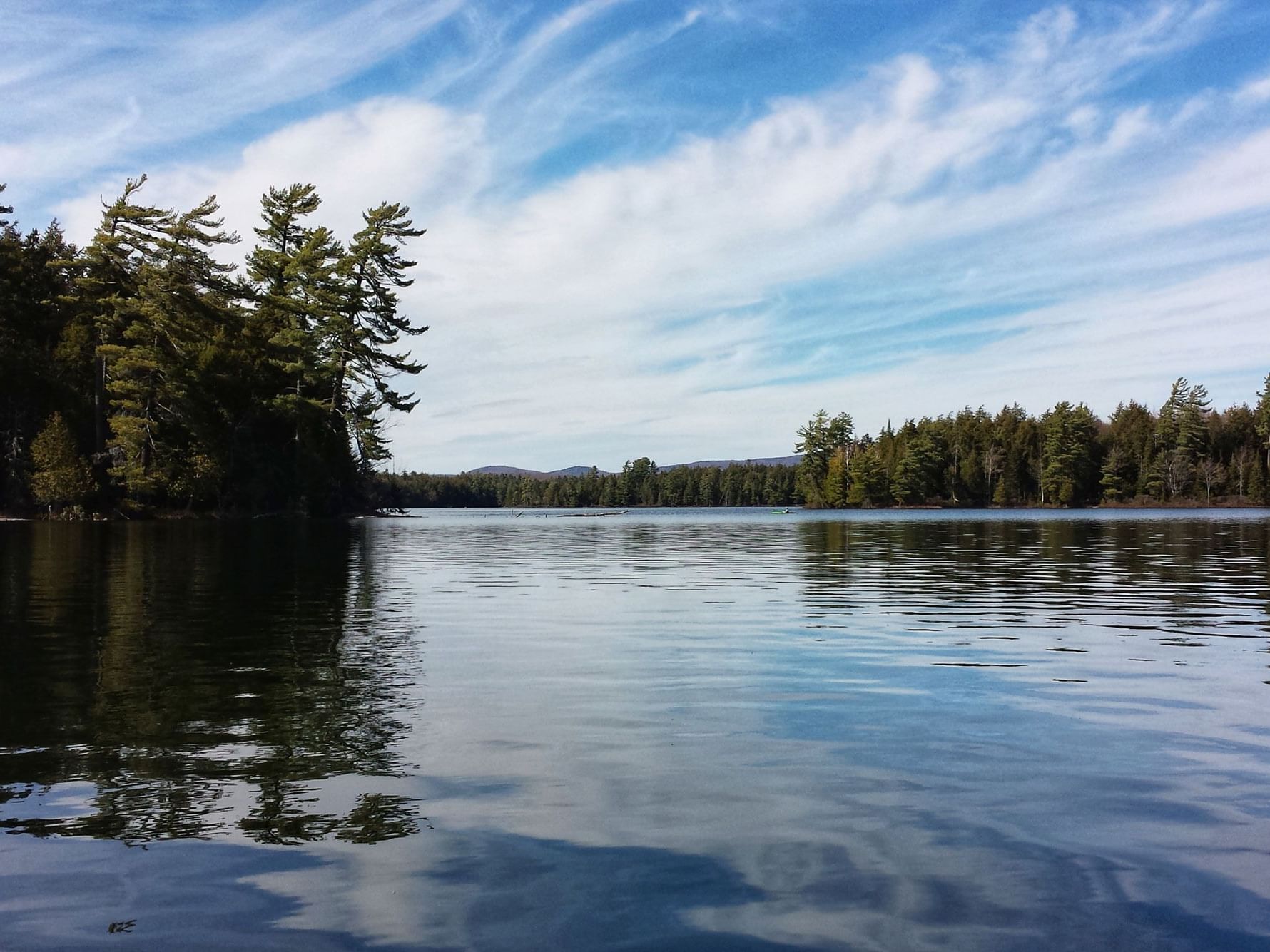 Tranquil lake reflecting a blue, cloudy sky with a treeline and mountains in the distance near High Peaks Resort