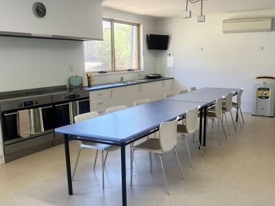 White kitchen with large ovens, dining area, and windows at La Trobe University - Orde House.