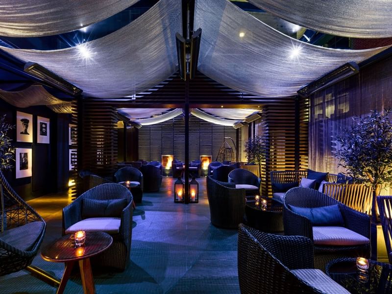 Elegant lounge with wicker chairs, candles, and drapes at The May Fair Hotel, London.