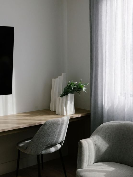 Sunset Junior Suite at Elysium Manly with white sculptural vases & greenery by a wooden desk under sheer curtains & a chair