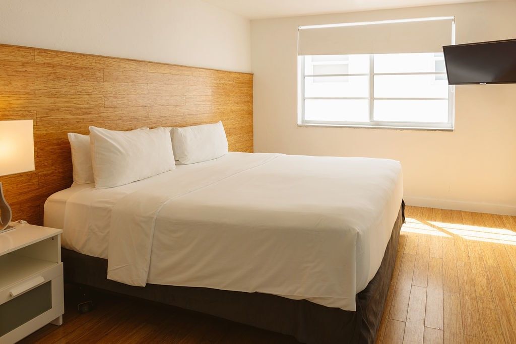 A wide view of a hotel room with a king-size bed, a window, and a flat-screen TV.