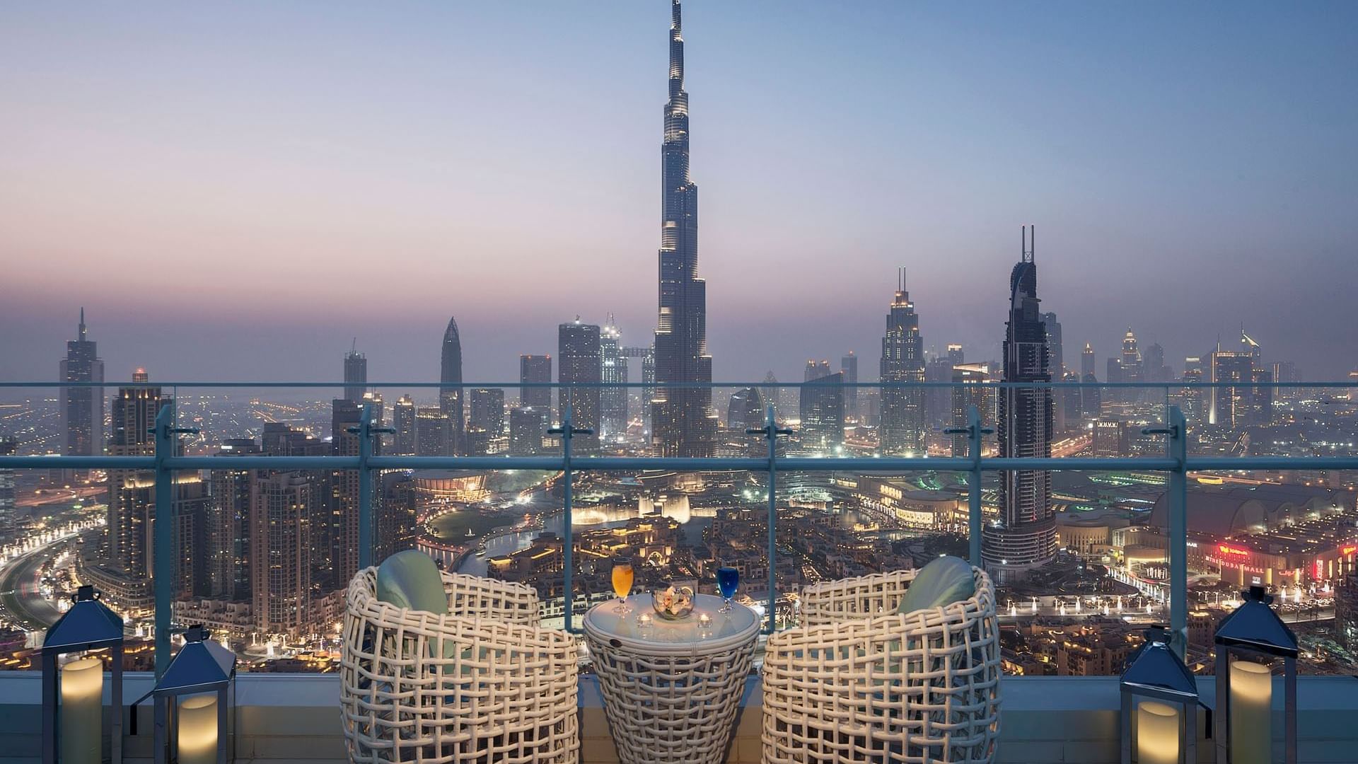 Night view of a balcony with wicker chairs overlooking the Burj Khalifa from Penthouse View at DAMAC Maison Distinction