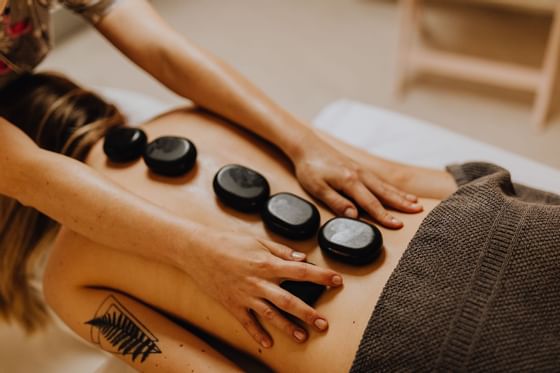 A woman is receiving a hot stone massage on her back from a therapist.
