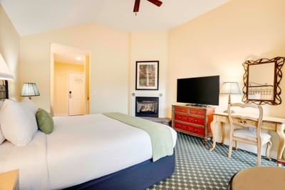 Cozy hotel room with bed, fireplace, desk, chair, and TV, creating a warm and inviting atmosphere.