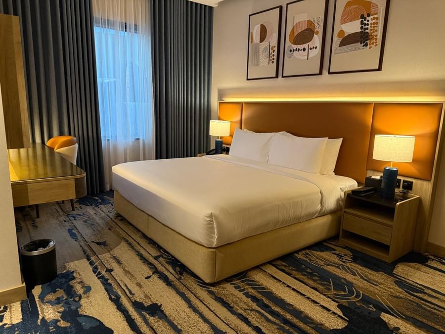 Bed between the side tables near the window and the work desk in the guest room at Warwick Jeddah Hotel & Spa