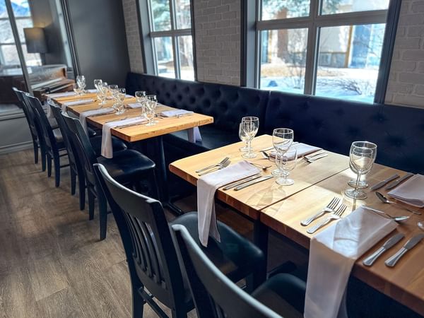 Elegant dining setup with wooden tables, black chairs, and large windows.