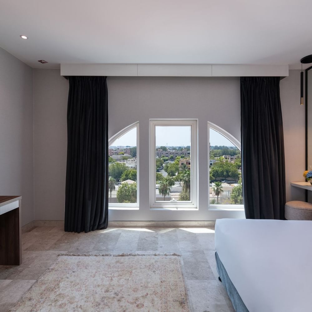 King bed with a wooden desk and TV near arched windows in Deluxe Room City View at Warwick Al Jubail