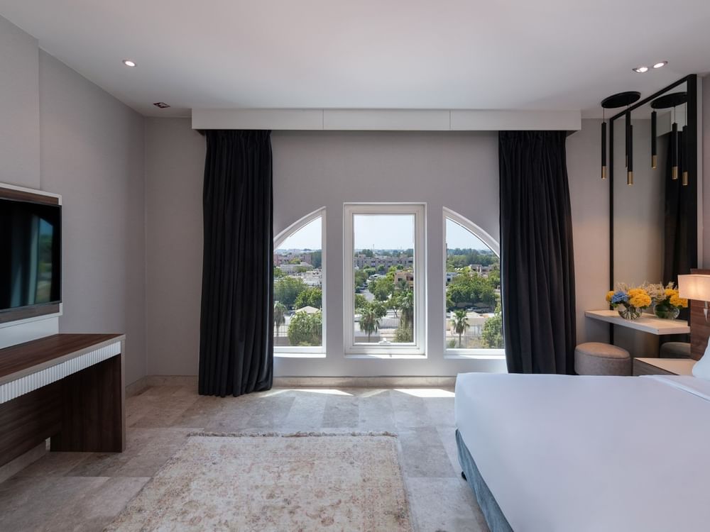 King bed with a wooden desk and TV near arched windows in Deluxe Room City View at Warwick Al Jubail