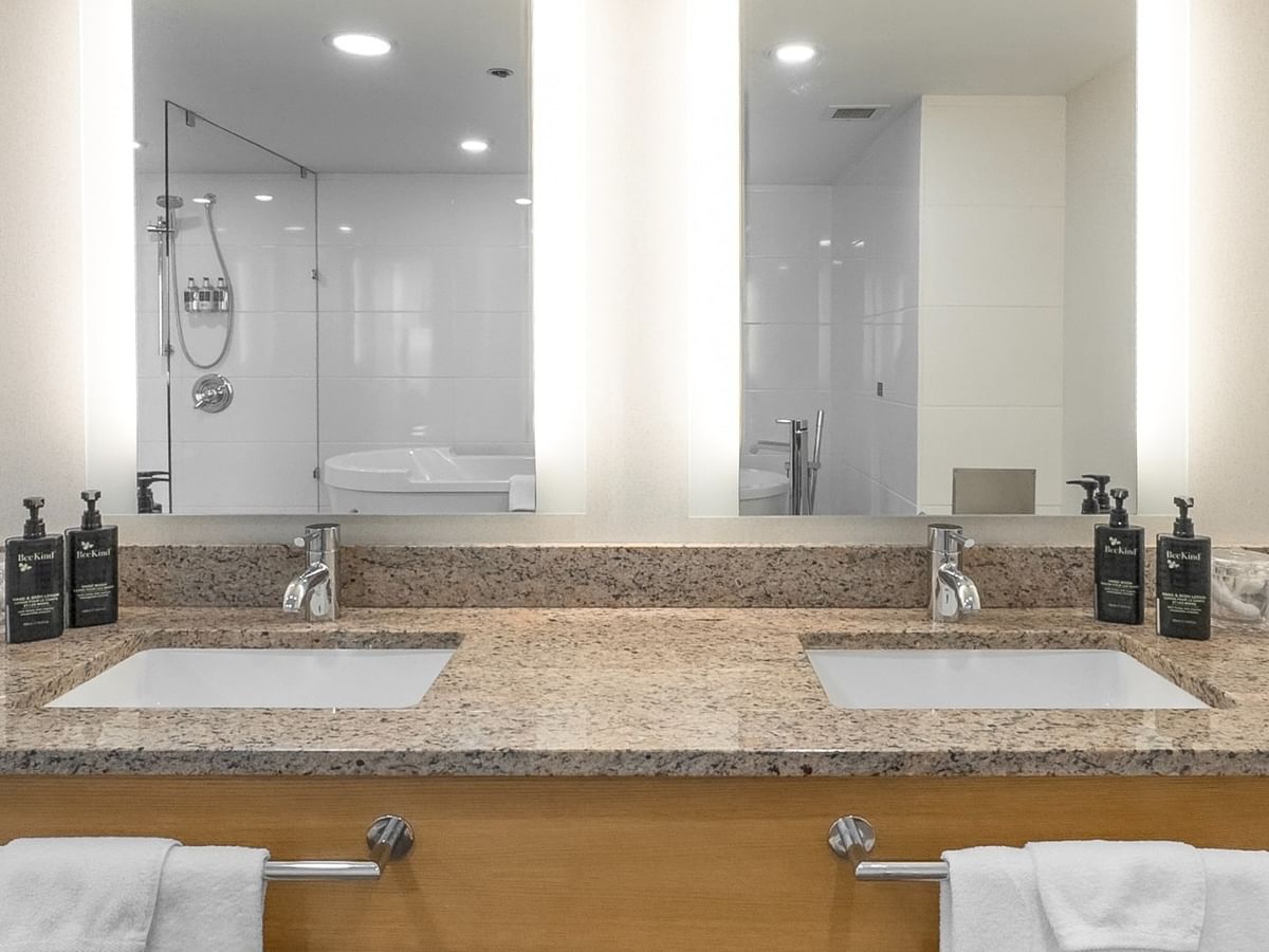 Two sinks with towels on a granite countertop, with a mirror showing the shower.