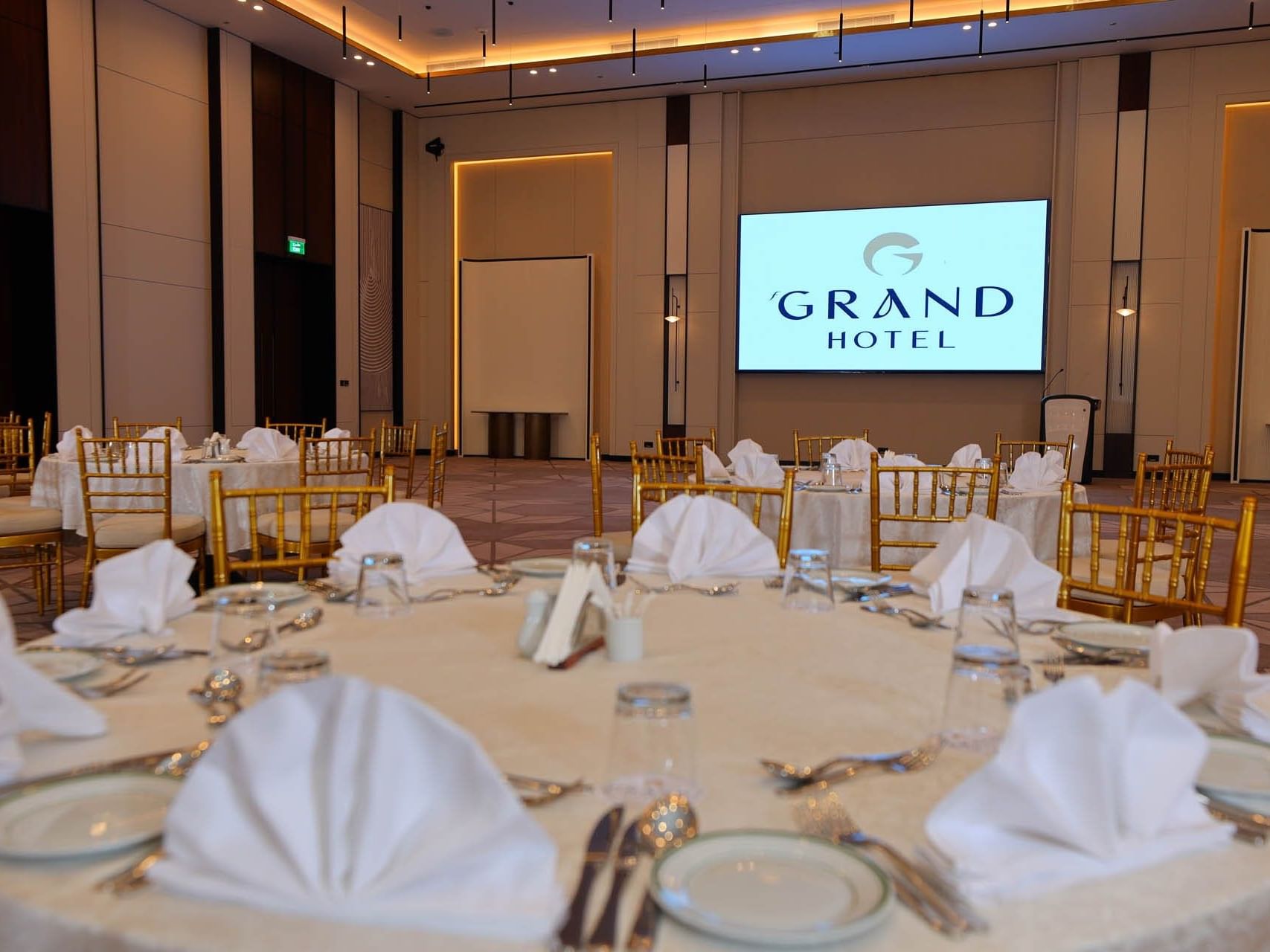 Banquet room with set tables, napkins, and a large screen reading 