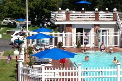 Loungers under umbrellas beside a sunlit pool, with people swimming and enjoying at Breezeway Boutique Hotel