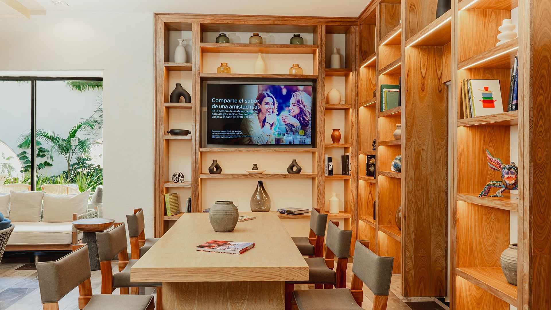 Dining table with cozy chairs, wall-mounted TV, and backlit shelves in Library Café & Deli at Camino Real Zaashila Huatulco