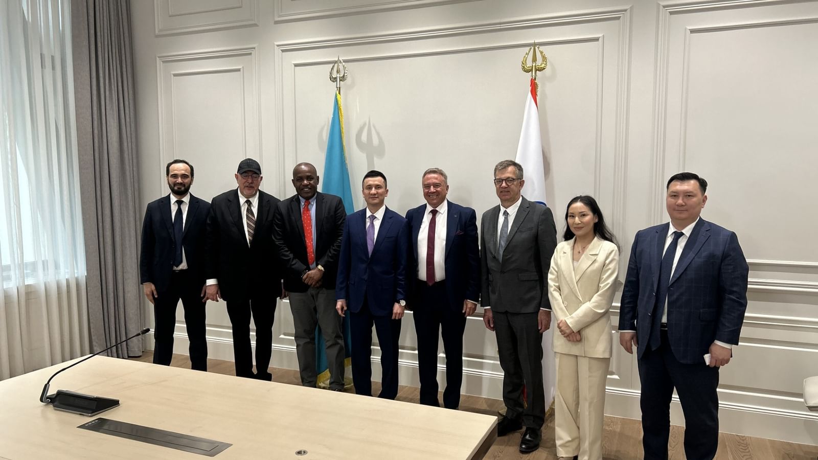 Business executives in formal attire pose for a group photo during a signing ceremony with national flags in the background.