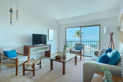 Living room with ocean view, balcony, sofa, chair, coffee table, TV, and tropical decor.