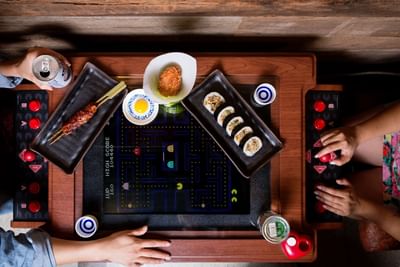 Two people playing Pac-Man while enjoying the food in Hojoko at The Verb Hotel