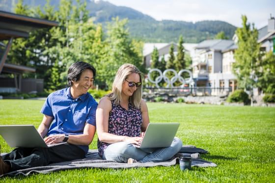 Two people sitting on the grass & working on their laptops near Blackcomb Springs Suites