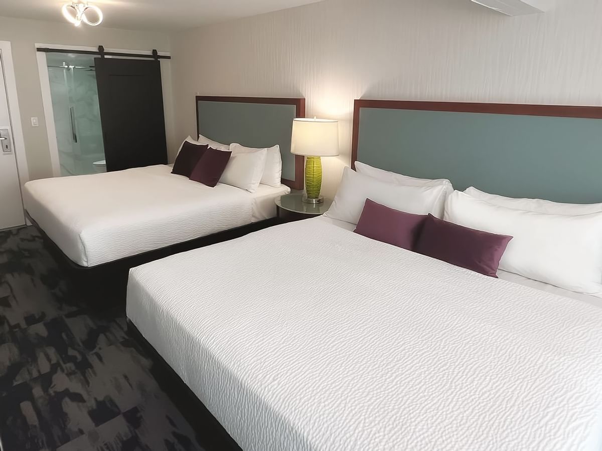 Guest room with two king beds, pillows, a desk, chair and toilet