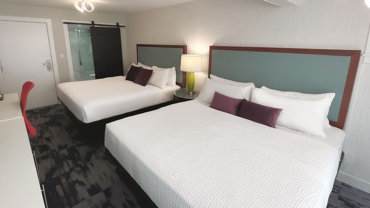 Guest room with two king beds, pillows, a desk, chair and toilet