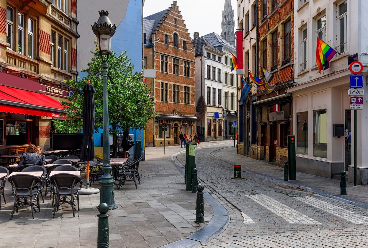 Outdoor seating with black chairs and tables by a red awning under a vintage street lamp near Warwick Grand Place Brussels