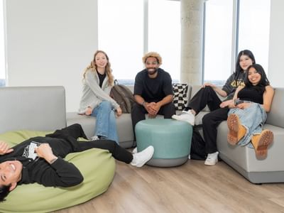 Smiling students hanging out in a clean and modern lounge with floor to ceiling windows.