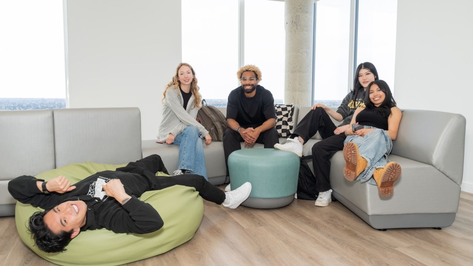 Smiling students hanging out in a clean and modern lounge with floor to ceiling windows.