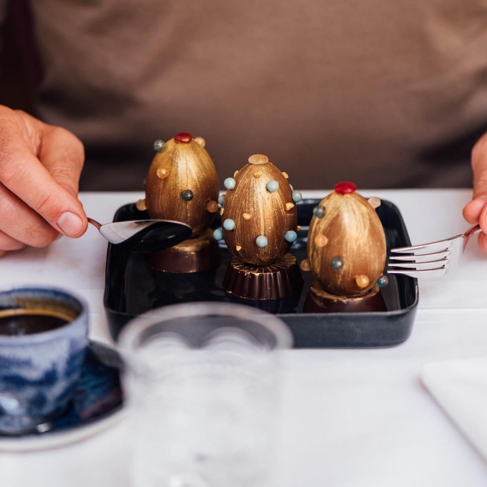 Tre cioccolatini decorati in un vassoio nero con forchette e tazza di caffè.