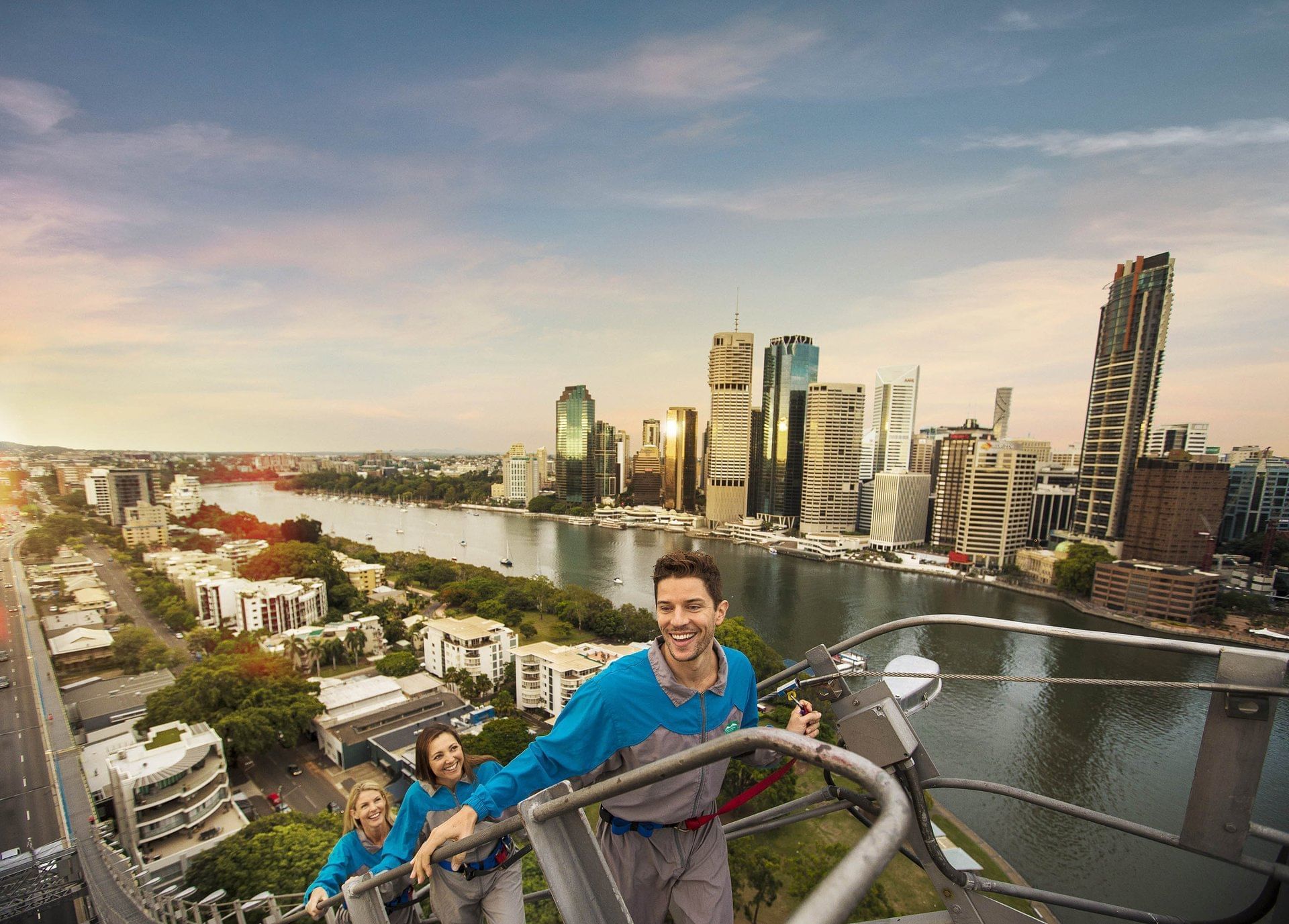 People climbing the Story Bridge with the sunlit Brisbane city skyline and river in the background near The Sebel Brisbane