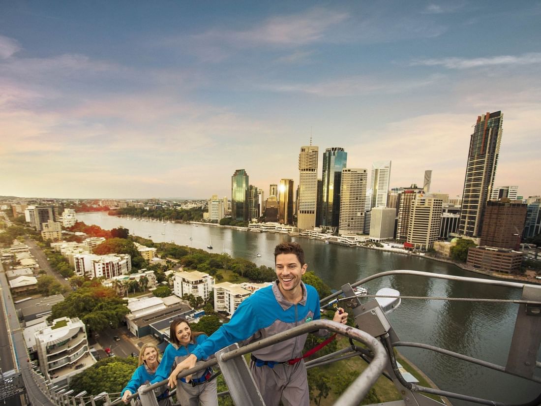 People climbing the Story Bridge with the sunlit Brisbane city skyline and river in the background near The Sebel Brisbane