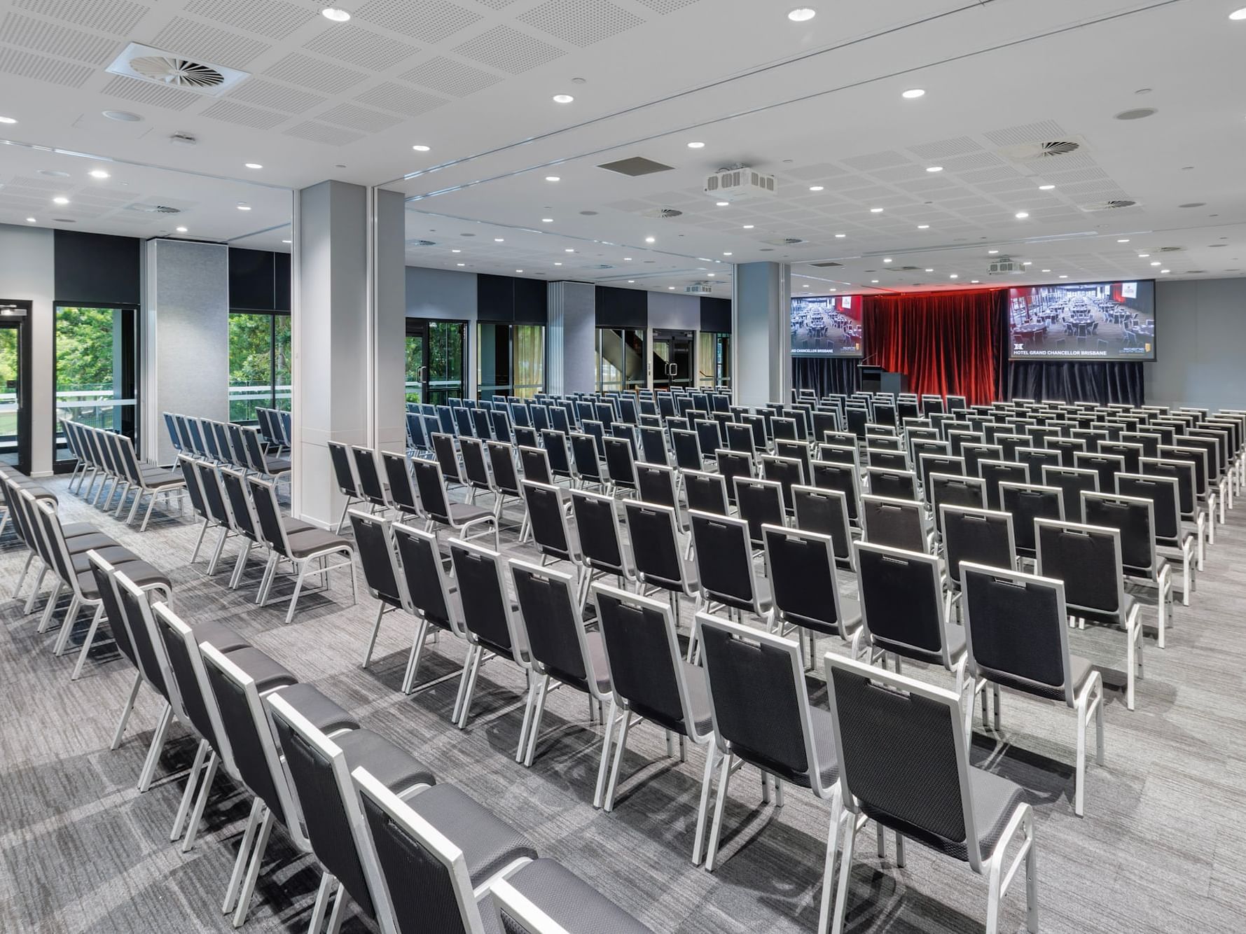 Large conference and event space set in theatre style with rows of chairs facing a stage and presentation screens at Hotel Grand Chancellor Brisbane.