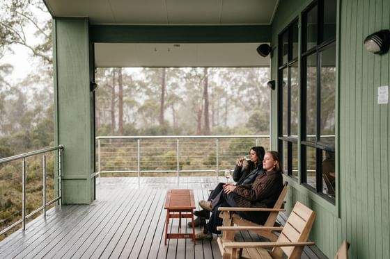 Two people relaxing on a porch with scenic forest view at Cradle Mountain Hotel