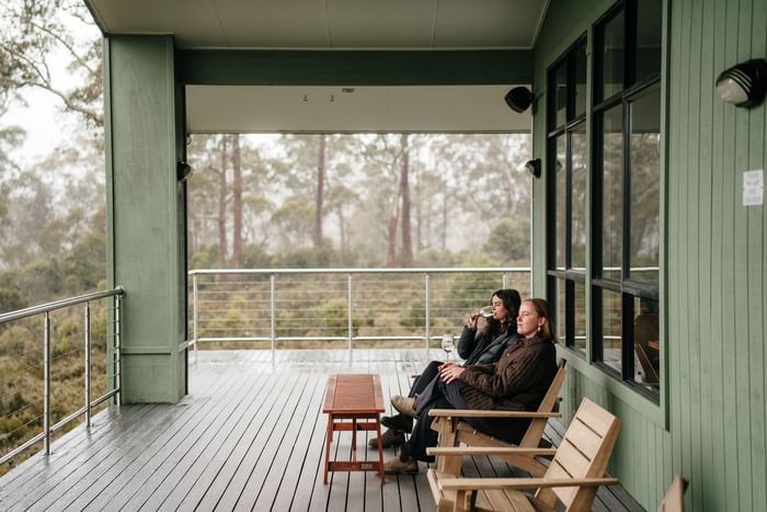 Two people relaxing on a porch with scenic forest view at Cradle Mountain Hotel