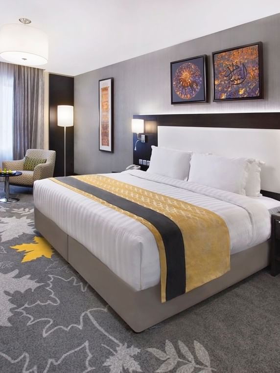 Work desk, nightstand, and cozy lounge chair by the bed in the Deluxe Room with carpeted floors at Warwick Hotel Jeddah