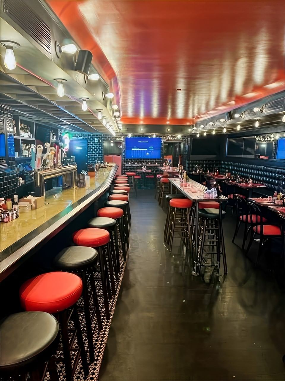 A dimly lit bar with red and black stools, tables, and chairs.