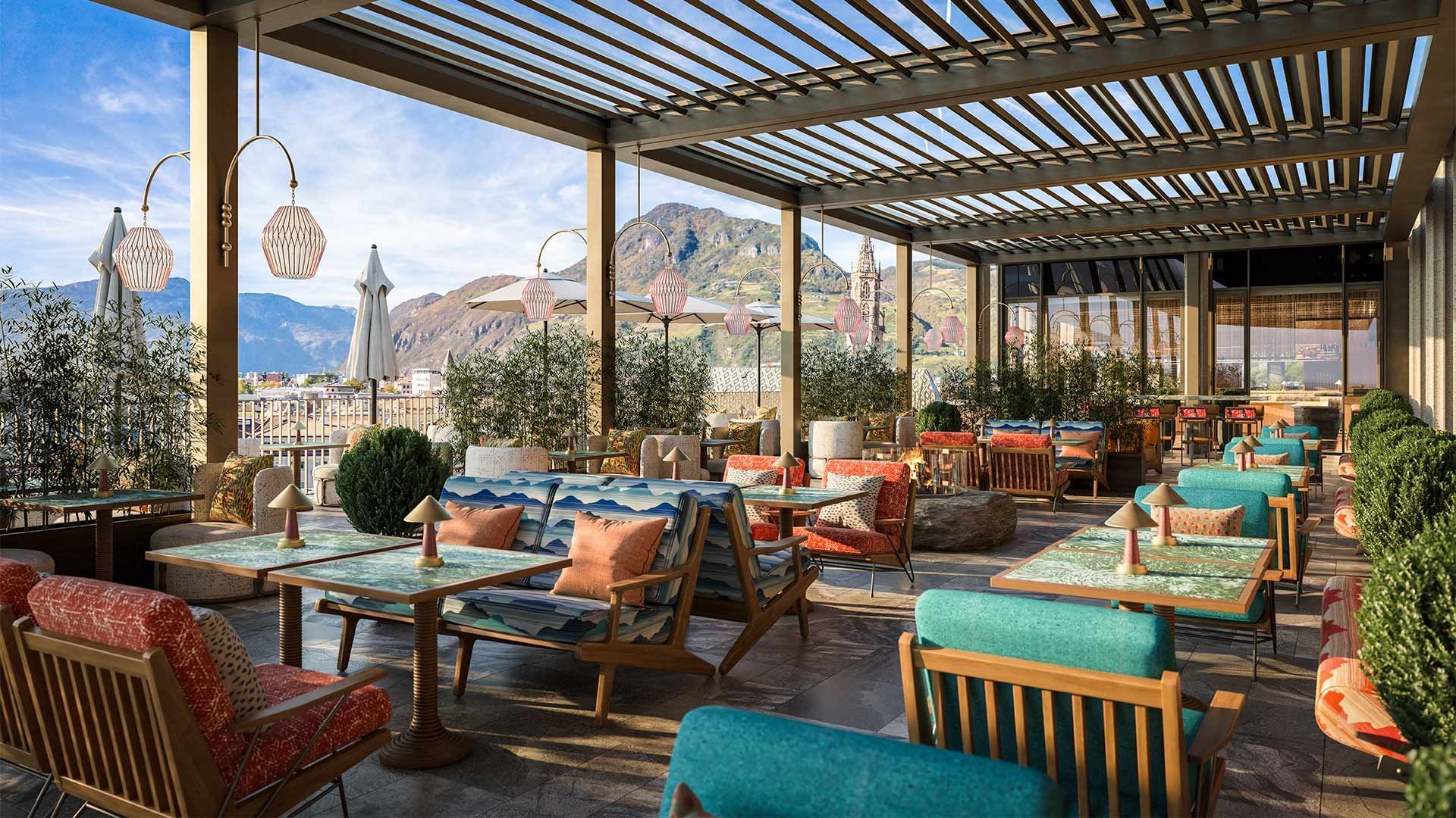 Terrazza esterna di un ristorante con mobili in legno e cuscini colorati, e vista sulle montagne.