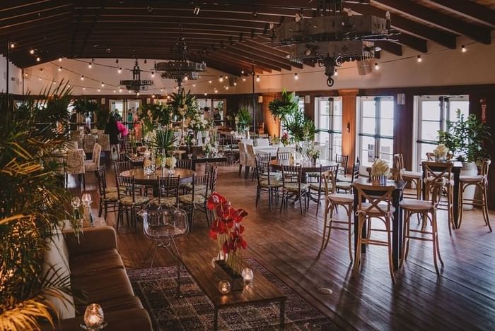 Elegant event space with exposed beam ceiling, string lights, and mixed seating arrangements at Tradewinds Apartment Hotel